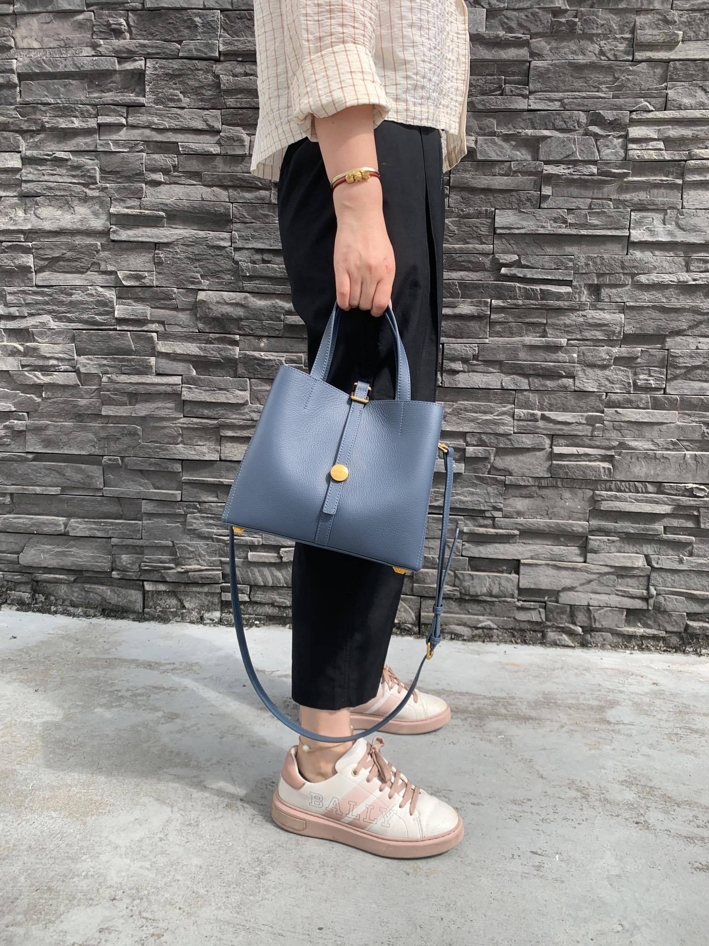 Person holding a blue handbag against a stone wall.