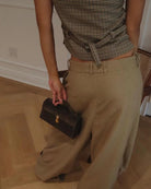 Person holding a black handbag wearing a plaid top and beige pants indoors.
