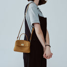 Person holding a brown handbag with a plain background