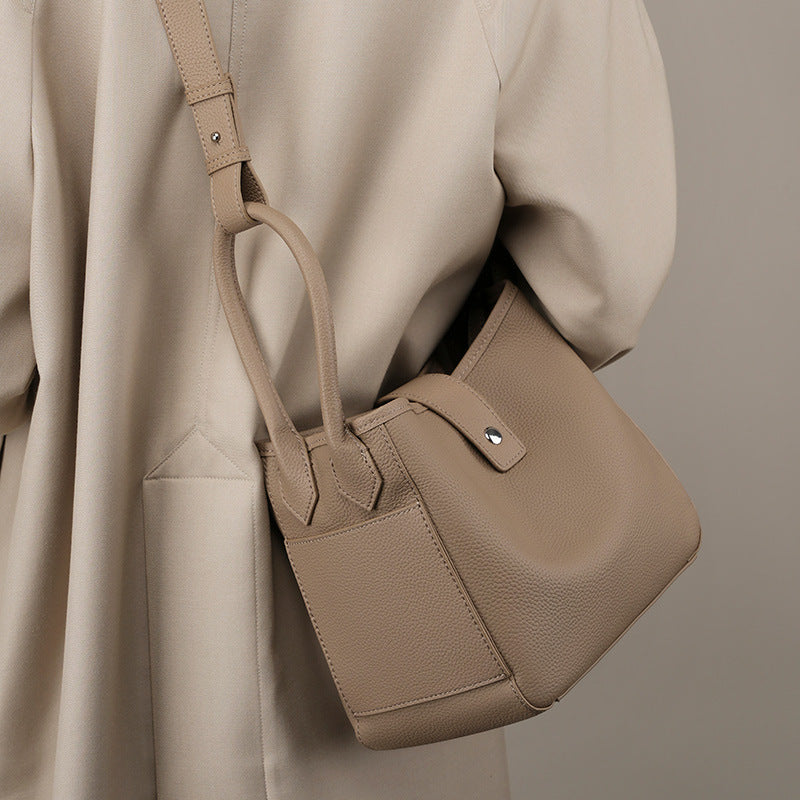 Beige handbag held by a person wearing a matching beige coat on a neutral background