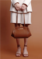 Person holding a brown handbag against a brown background
