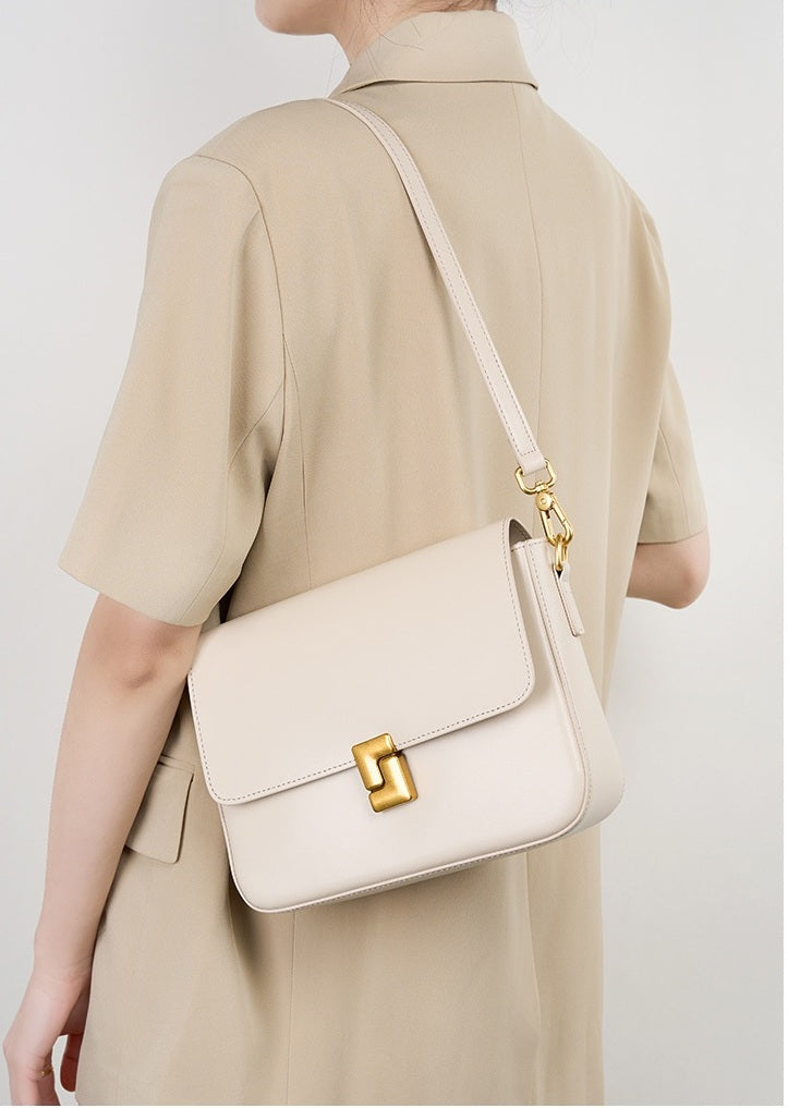 Person wearing a beige outfit with a matching handbag on a plain background