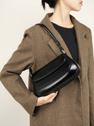 Person holding a black handbag against a neutral background