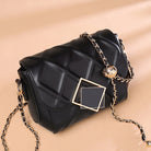 Black handbag with gold chain strap on a beige background