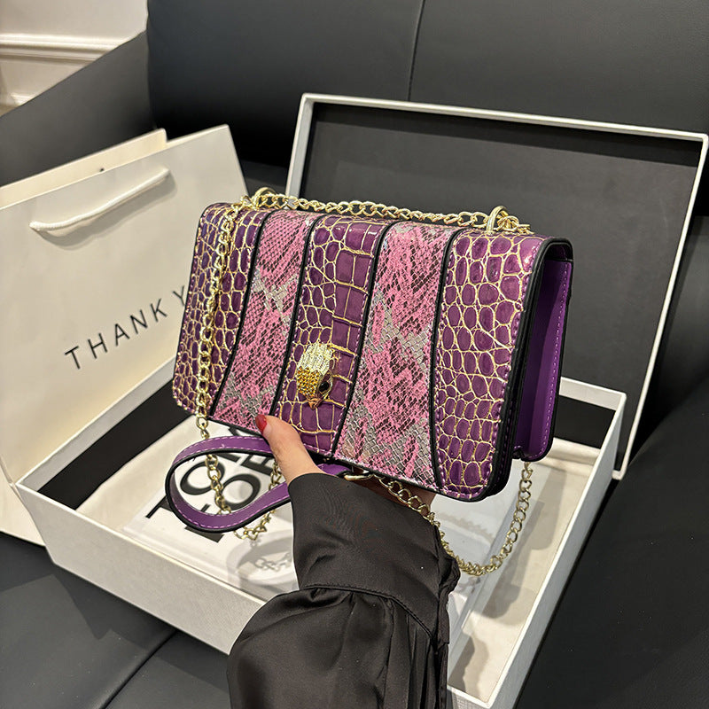 Purple and pink handbag with gold chain held by a hand, displayed in an open box.