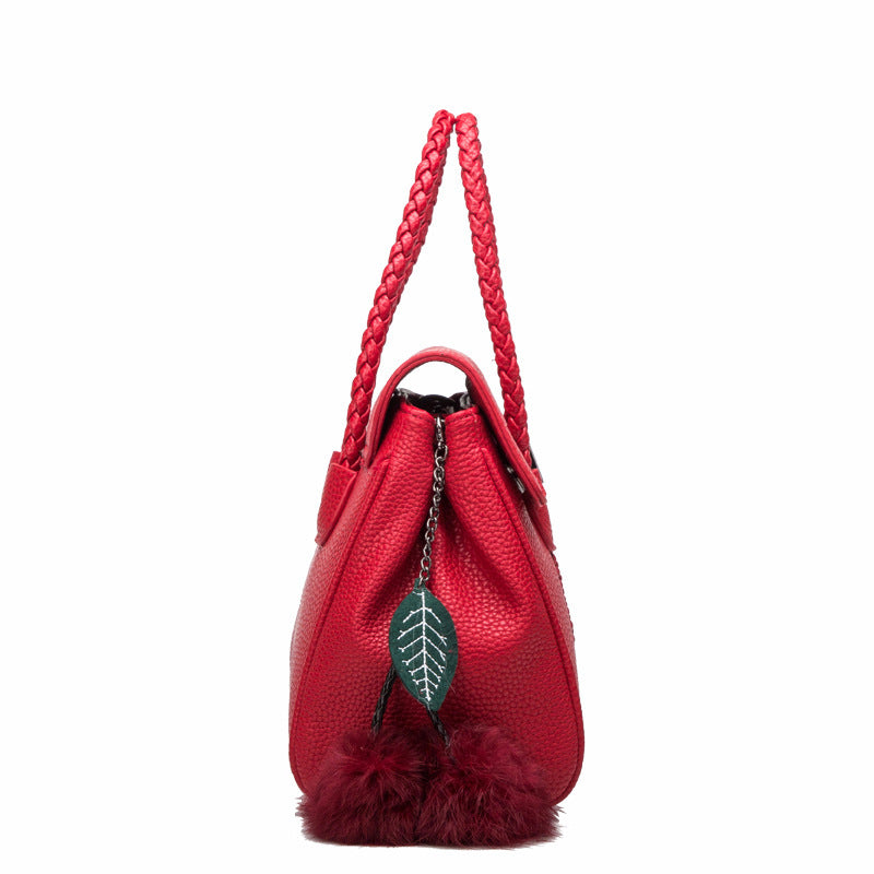 Red handbag with braided handle and leaf detail on a white background