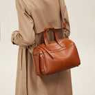 Brown leather handbag held by a person wearing a beige coat on a light background
