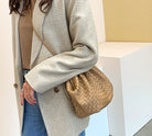 Person wearing a plaid coat with a woven handbag against a neutral background