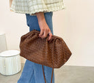 Person holding a brown woven handbag indoors