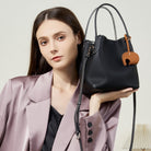 Woman holding a black handbag with a brown tag against a neutral background