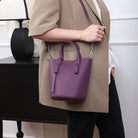 Person holding a purple handbag with a neutral background
