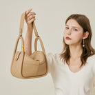 Woman holding a beige handbag against a plain background