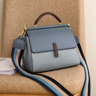 Blue handbag with a brown handle and strap on a beige surface