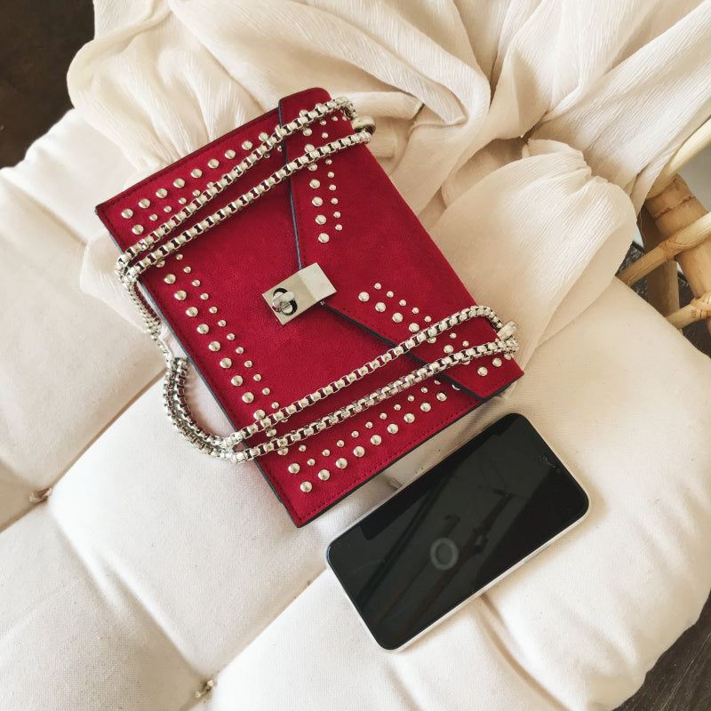 Red studded handbag with a chain detail on a white cushion next to a smartphone.
