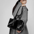 Woman holding a black leather handbag against a plain background