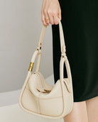 Beige handbag held by a person against a neutral background