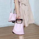 Person holding a pink handbag with a unique design, wearing a beige dress.