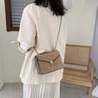 Person holding a beige handbag with a chain strap in a room with a wooden chair.