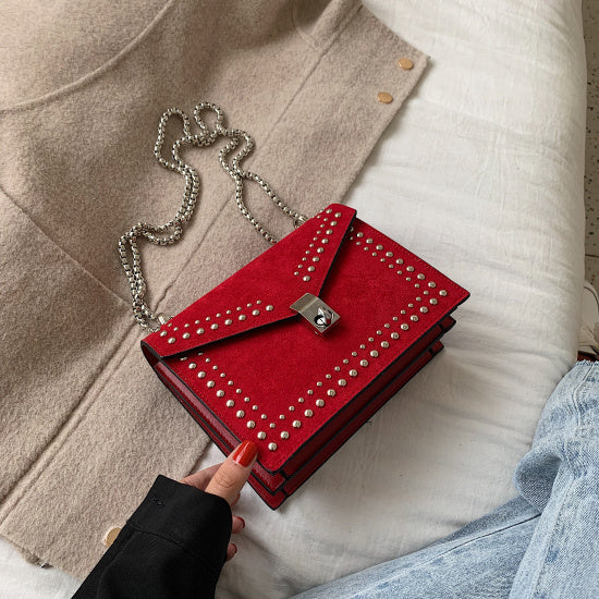 Red studded handbag held by a hand on a neutral background