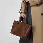 Person holding a brown leather handbag with a beige coat