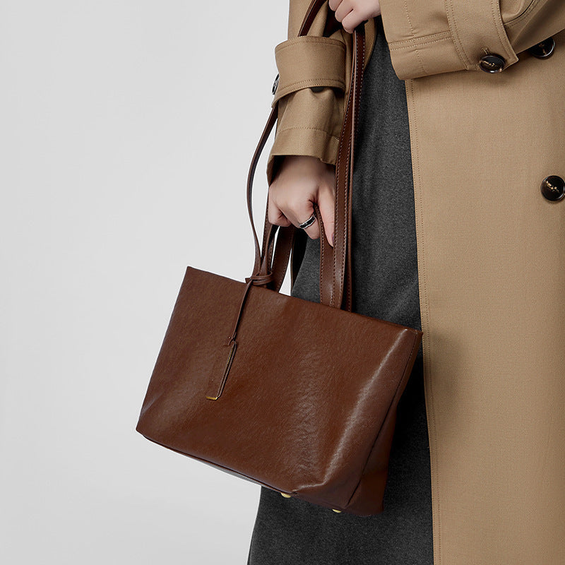 Person holding a brown leather handbag with a beige coat