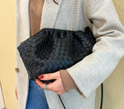 Person holding a black woven clutch against a neutral background
