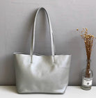 Silver handbag on a white surface with a gray wall and plant in the background