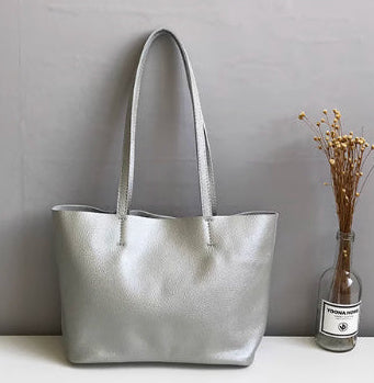 Silver handbag on a white surface with a gray wall and plant in the background