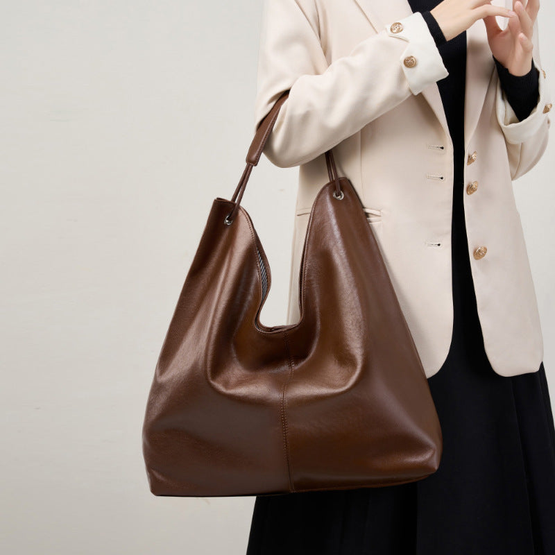 Brown leather handbag held by a person wearing a beige blazer against a neutral background