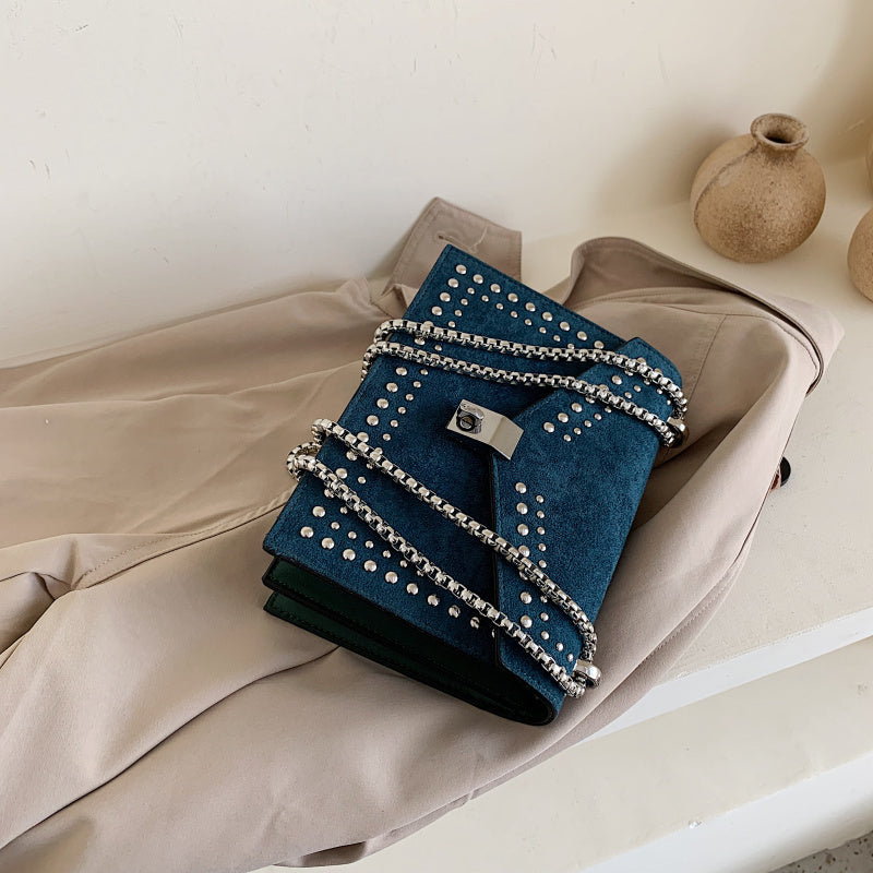 Blue studded handbag with chain detail on a beige surface