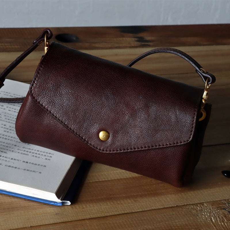 Brown leather clutch bag on a wooden surface with an open book underneath
