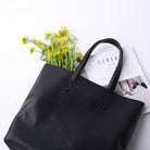Black tote bag with yellow flowers and a magazine on a white background