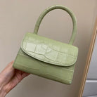 Green handbag with crocodile texture held by a hand against a neutral background