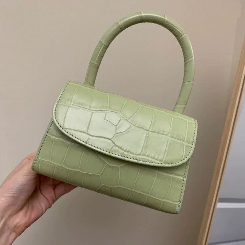 Green handbag with crocodile texture held by a hand against a neutral background