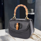 Black handbag with bamboo handle and accents on a wooden surface