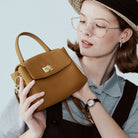 Woman holding a brown handbag against a light blue background