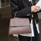 Person holding a brown leather handbag with a blurred background