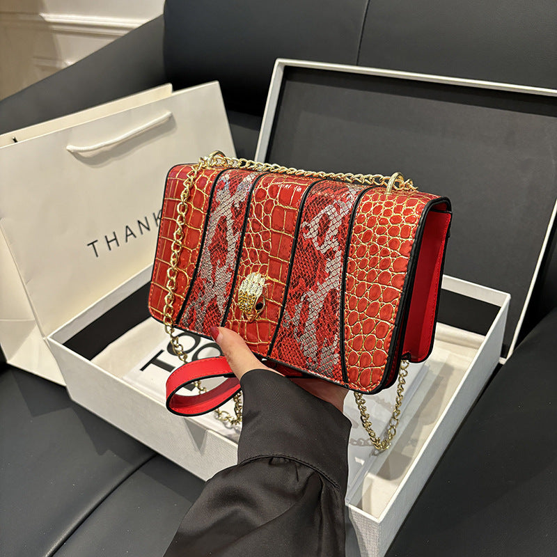 Red crocodile-patterned handbag with gold chain held by a person, displayed against a black background.