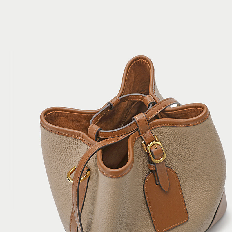 Beige leather handbag with brown accents on a light gray background