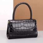 Black crocodile-patterned handbag on a white surface with a beige background