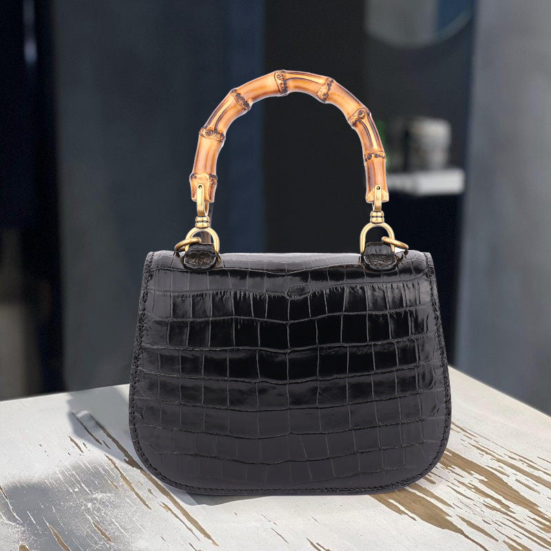 Black textured handbag with a gold bamboo handle on a wooden surface.