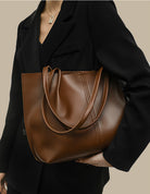 Person holding a brown leather handbag against a neutral background