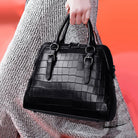 Black textured handbag held by a person against a red background