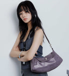 Woman holding a purple handbag against a plain background