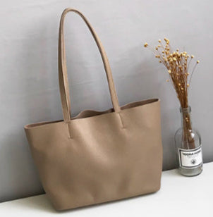 Beige tote bag on a white surface with a gray wall and plant in the background
