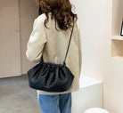 Person wearing a beige coat and blue jeans with a black woven handbag.