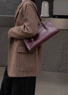 Person wearing a brown coat holding a maroon handbag in an indoor setting.