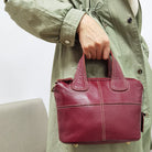 Person holding a red leather handbag with a light green coat