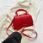 Red handbag held by a hand with a white coat and book in the background