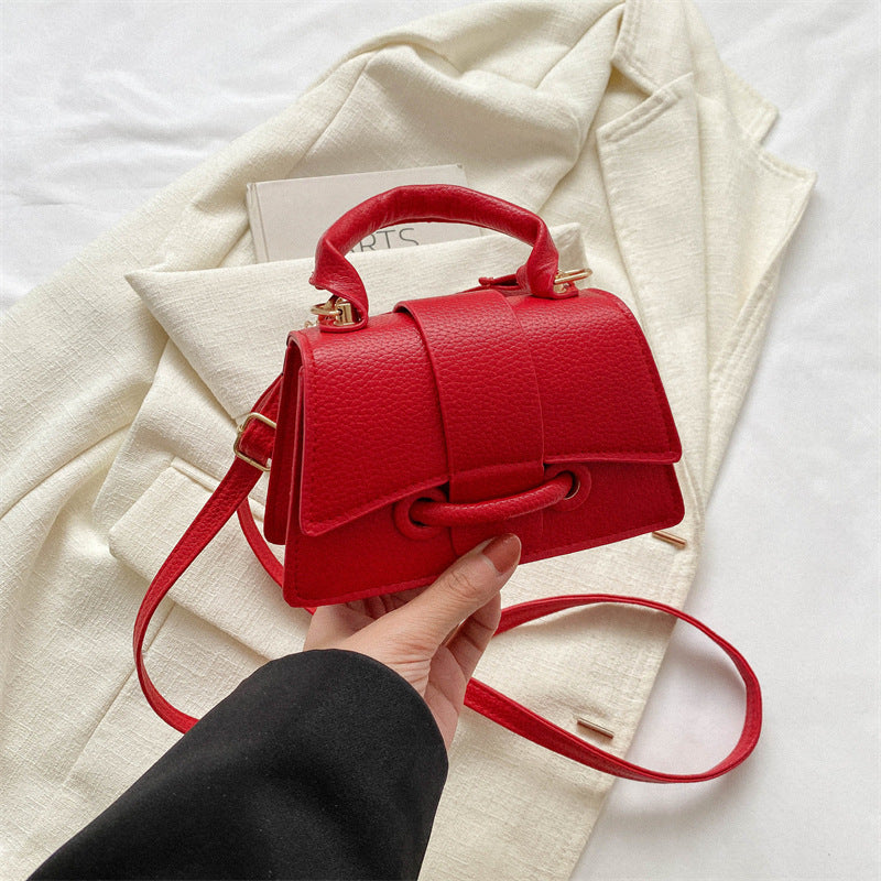 Red handbag held by a hand with a white coat and book in the background